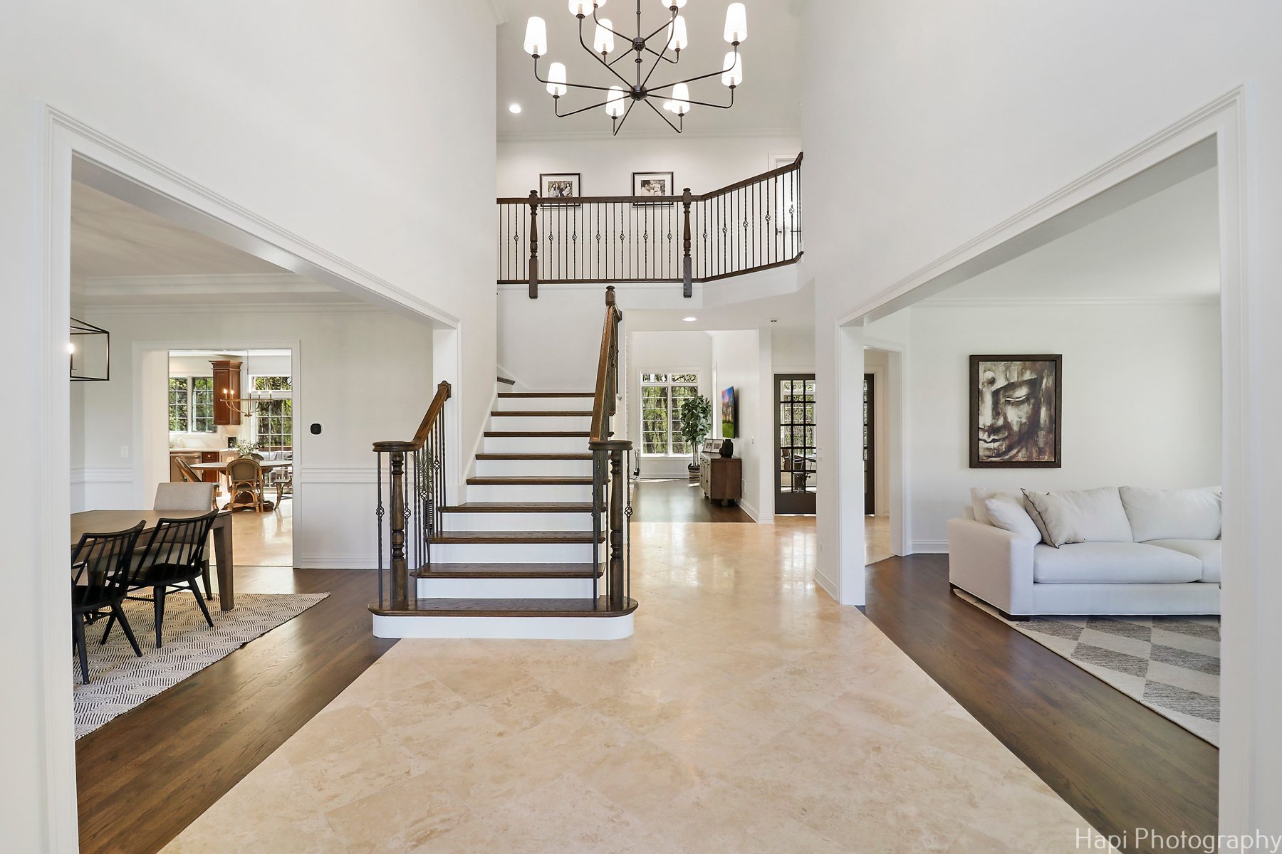 Two-story foyer with travertine floor, a wood and iron staircase and a modern chandelier