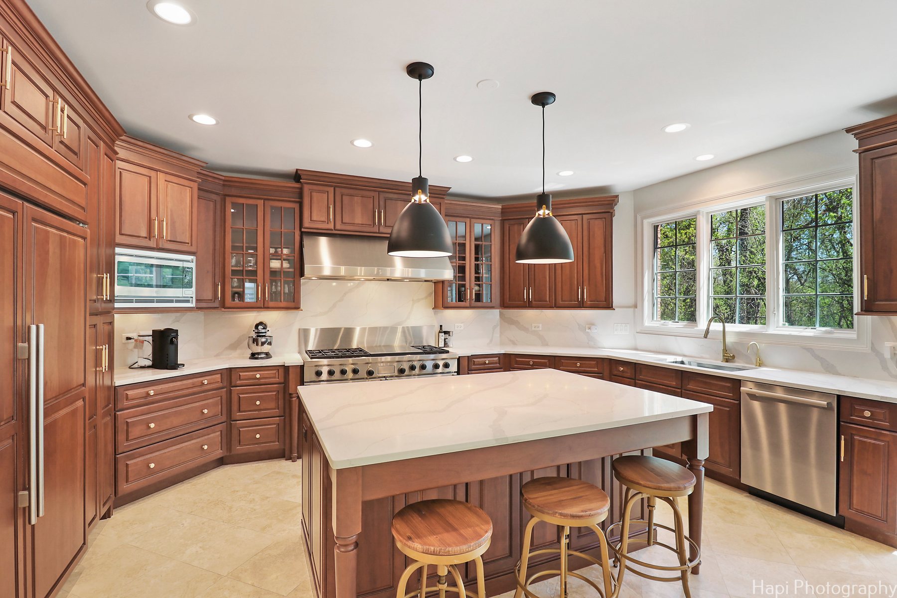 Cherry-cabinet kitchen with quartz counters and backsplash, black dome pendants and brass hardware