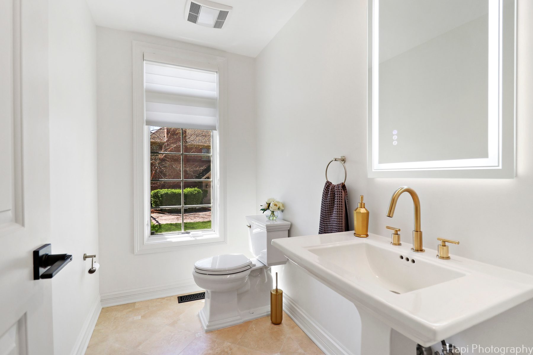 Powder room with a pedestal sink, brushed-brass faucet and backlit mirror