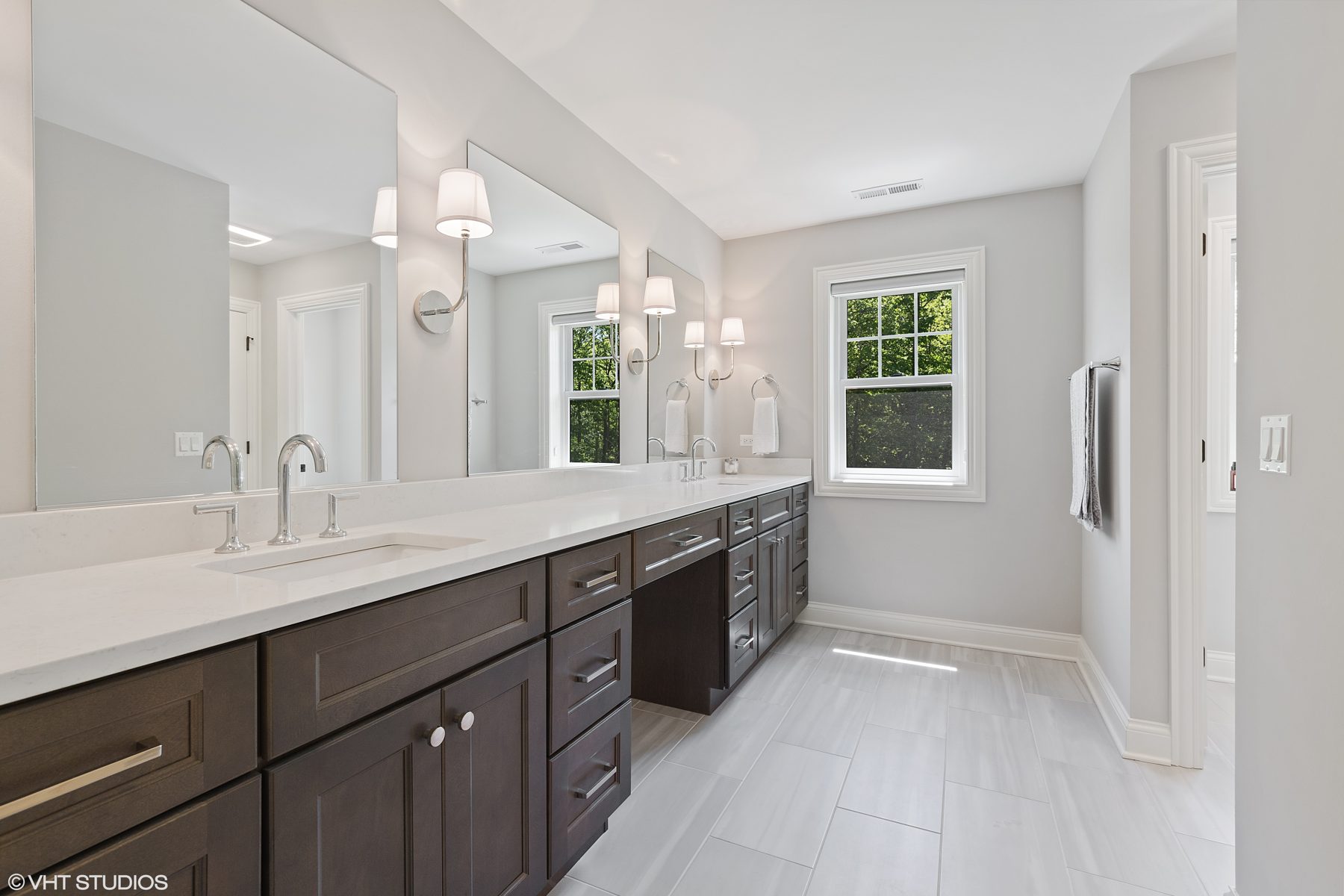 Primary bath with a long espresso vanity, makeup station, quartz counters and shaded sconces