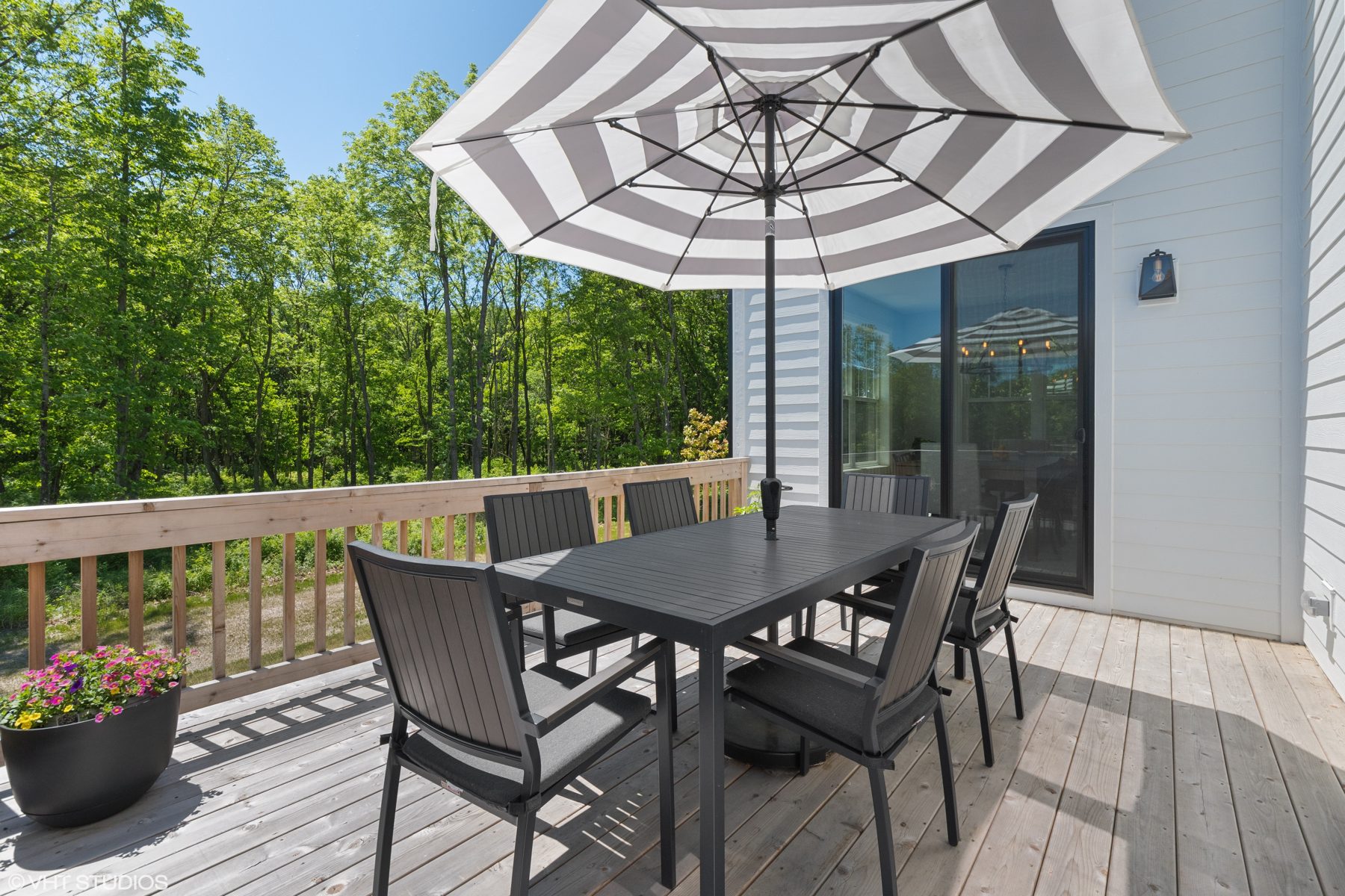 Cedar deck with a dining table and striped umbrella overlooking the woods